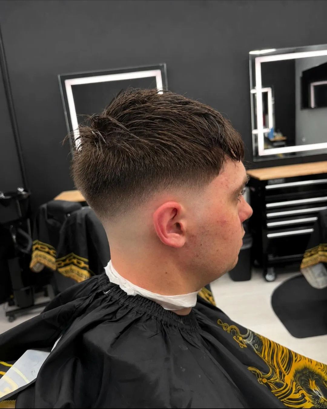 Side-view haircut in a barbershop, showing a fresh fade with a mirror and styling station in the background.